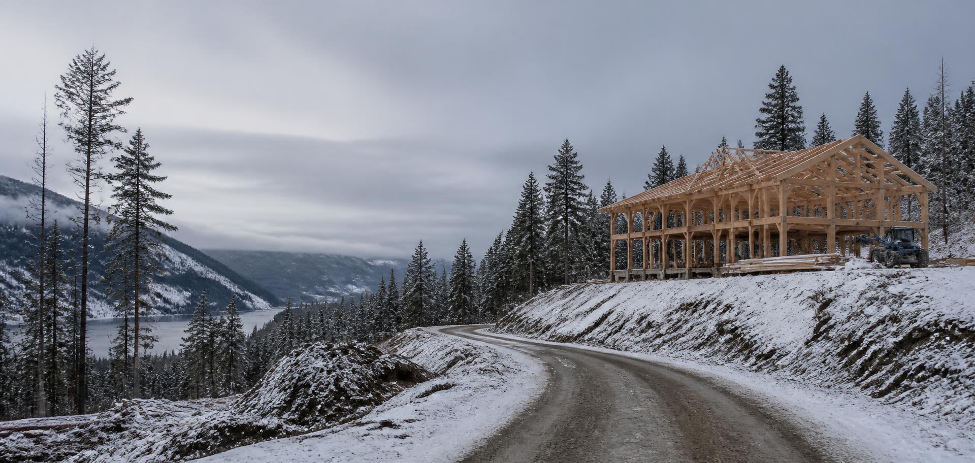 Snowy gravel mountain road beside a timber-framed building under construction in North Idaho